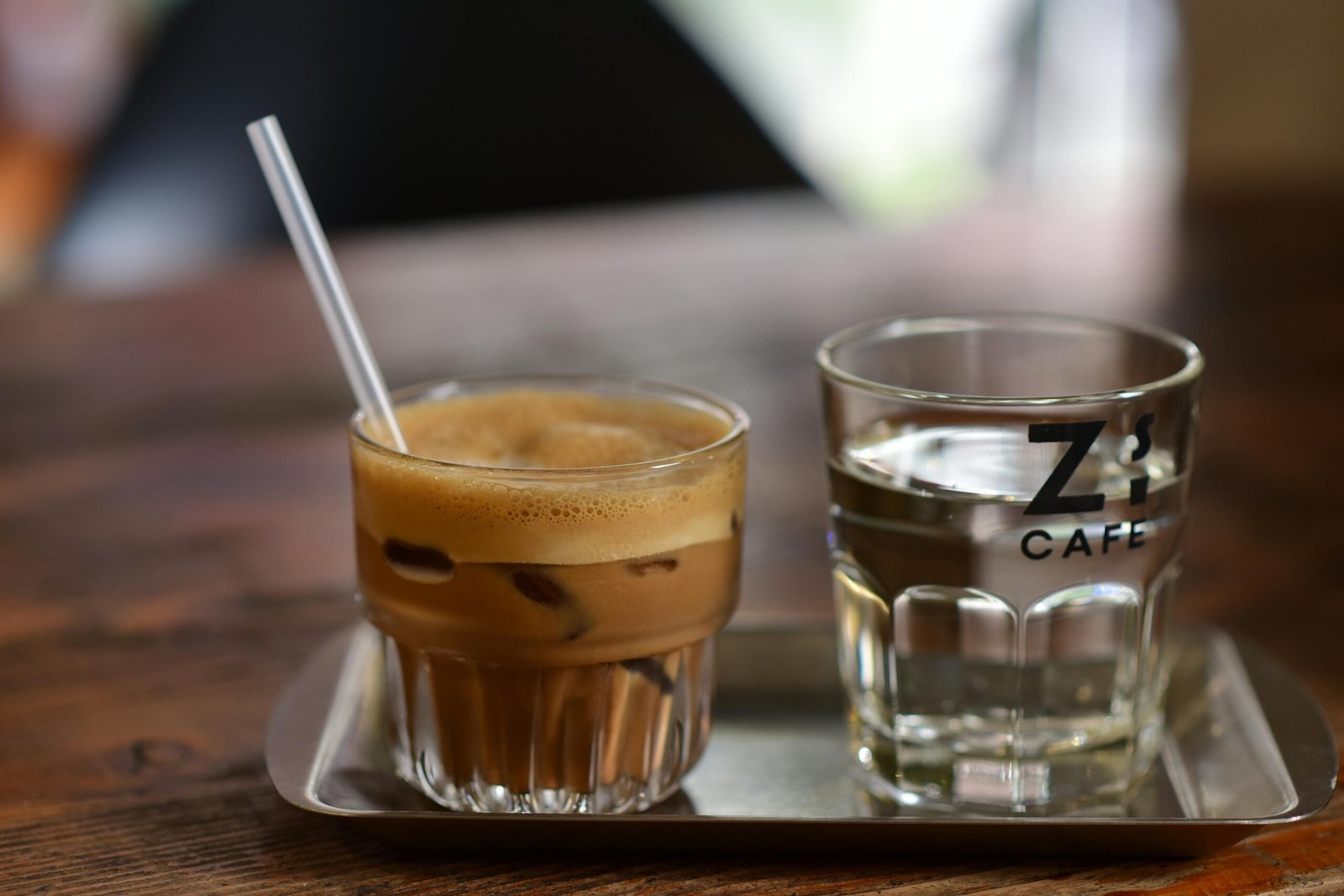 Refreshing iced coffee and water on a tray at a cafe with wooden table.